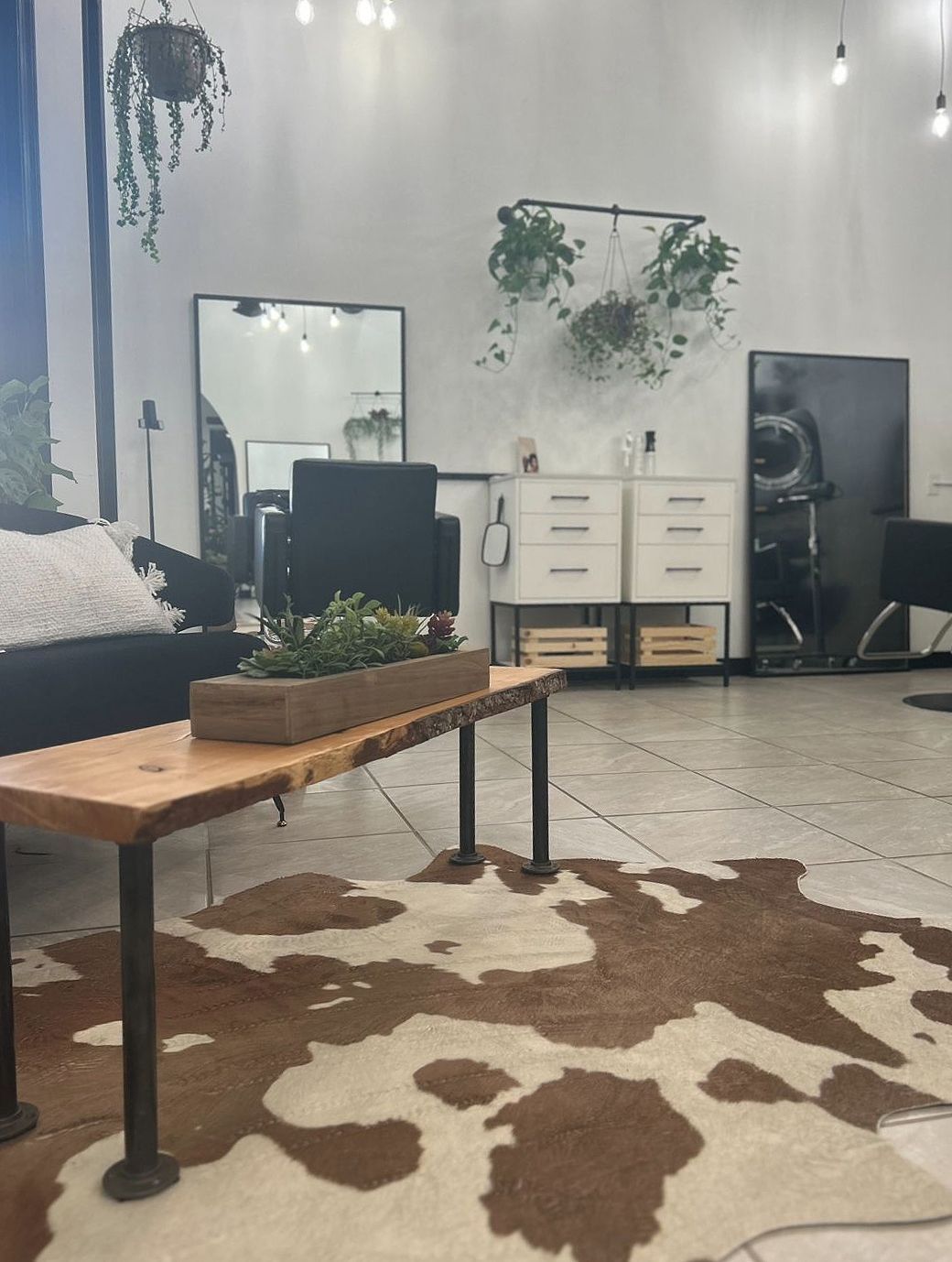Hair salon interior with a cowhide rug, wooden coffee table, and hanging plants.
