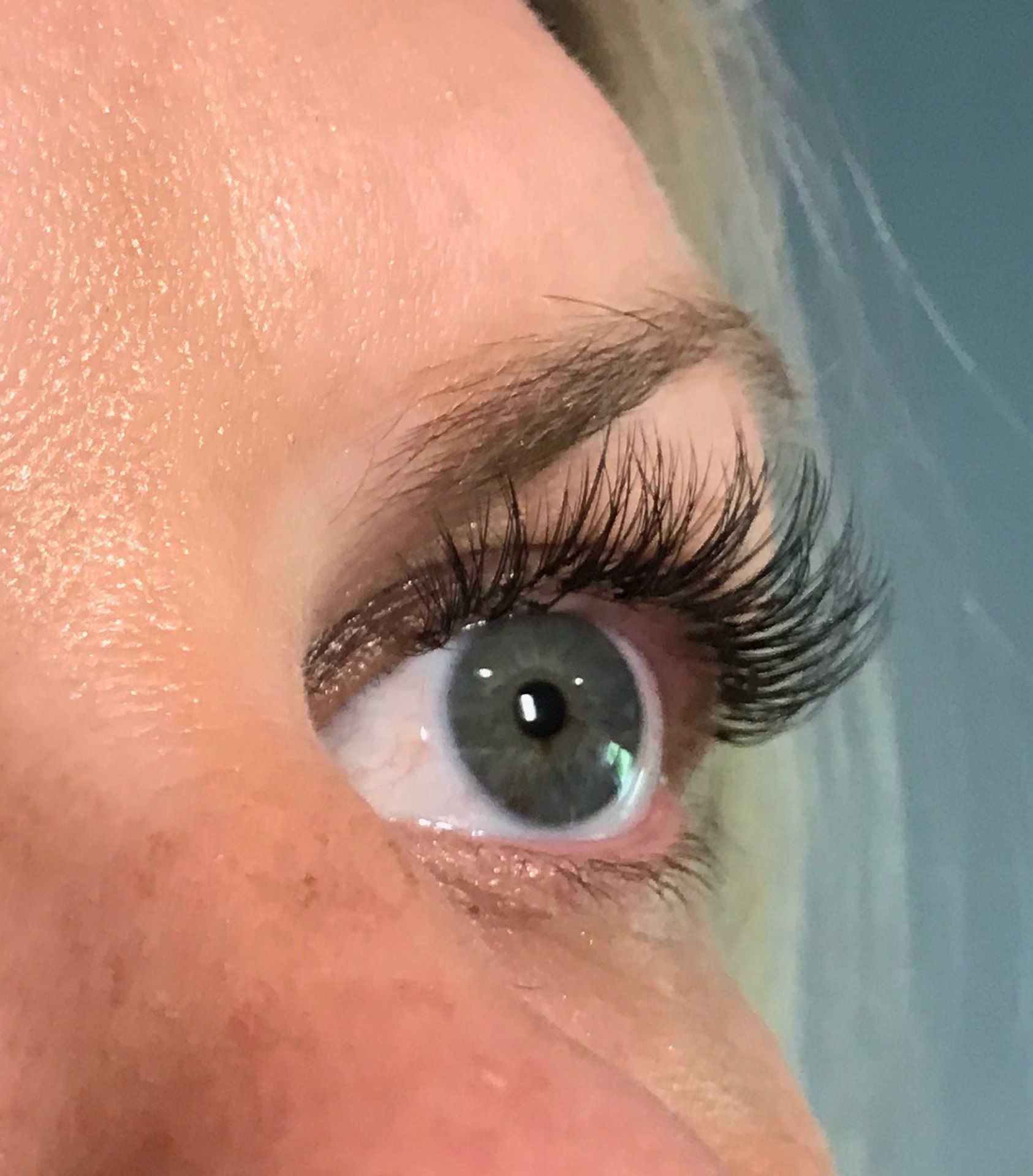 Close-up of an eye with long, dark eyelashes. Light blue eye, slightly open, looking upwards.