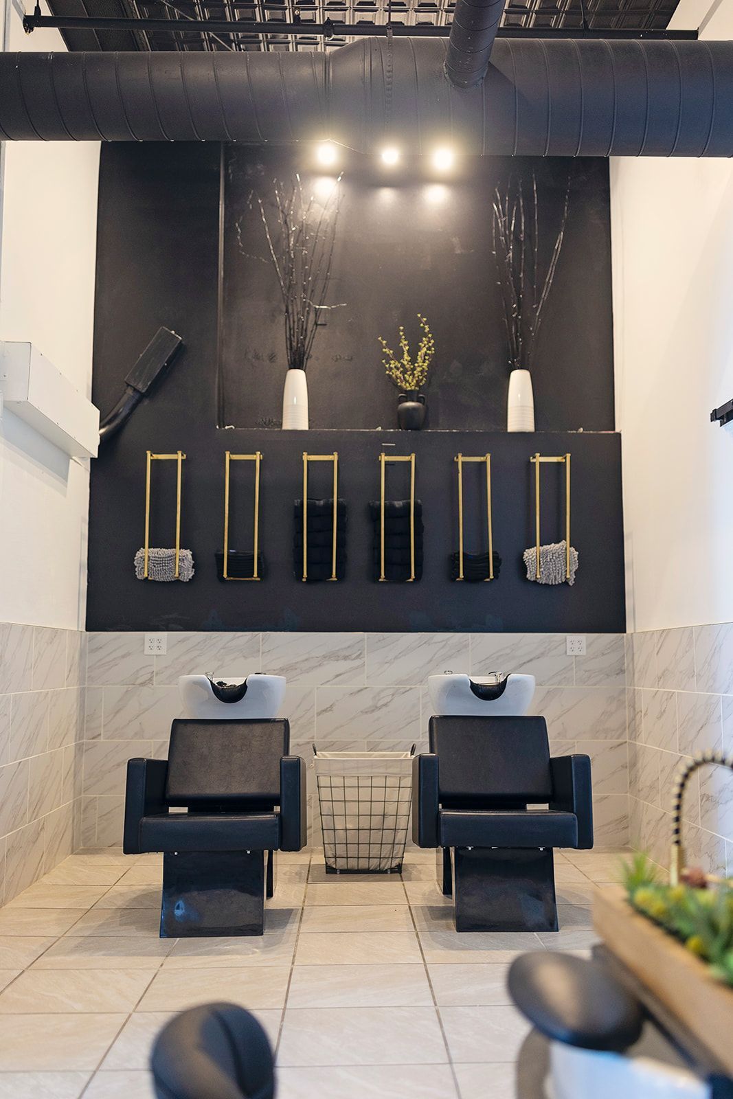 hair salon with two shampoo chairs facing a black wall with mirrors and decorative vases