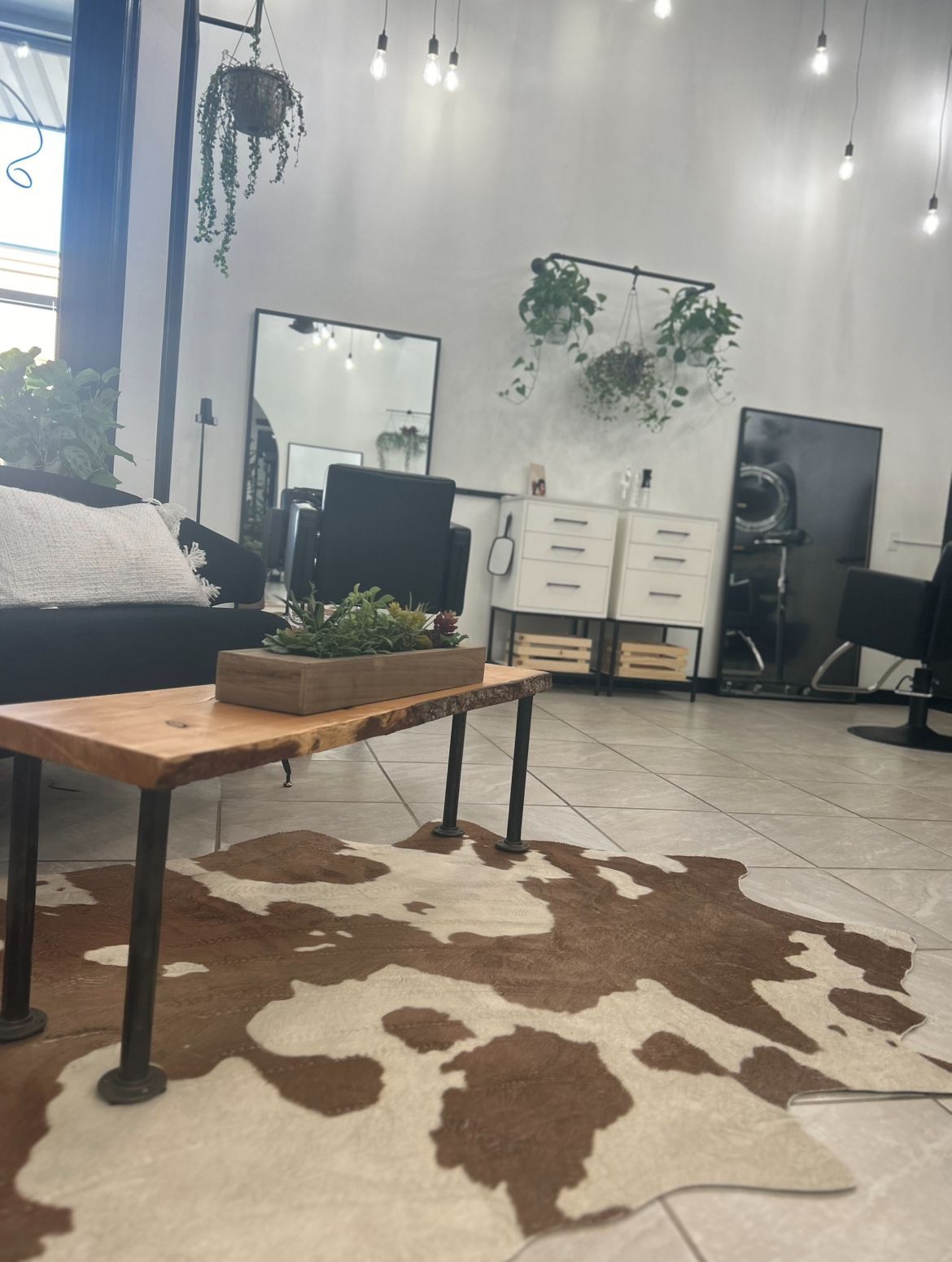 hair salon interior with couch, wooden coffee table, cowhide rug, mirrors, and hanging plants