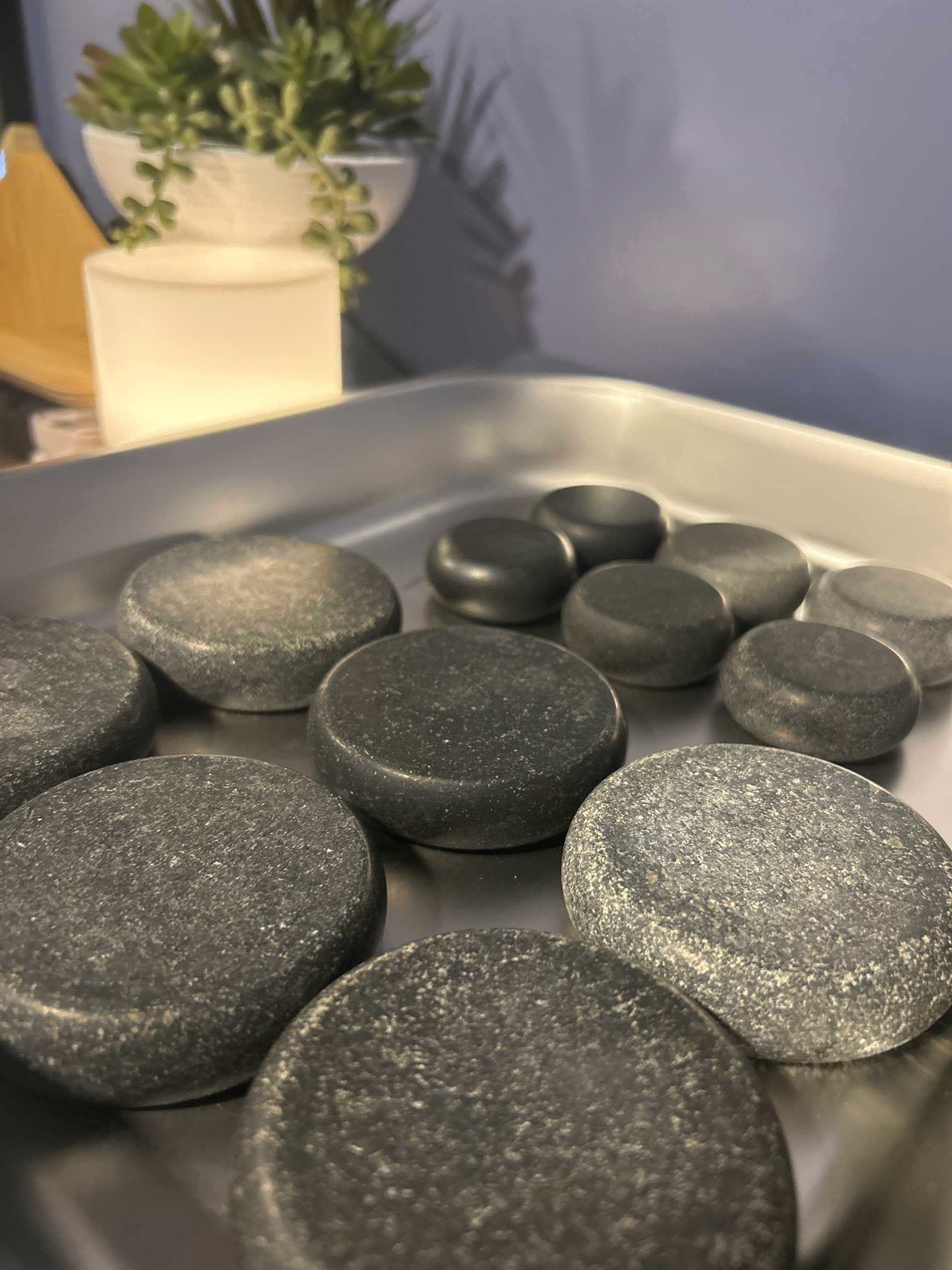 hot massage stones in a metal tray, with a plant and candle in the background