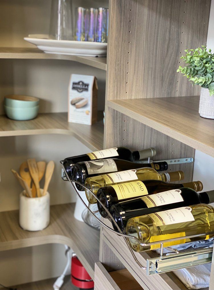 A bunch of wine bottles are sitting on a shelf in a pantry.