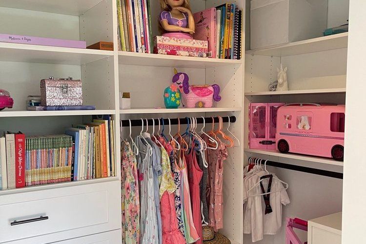 A closet filled with clothes , books , and a pink bus.