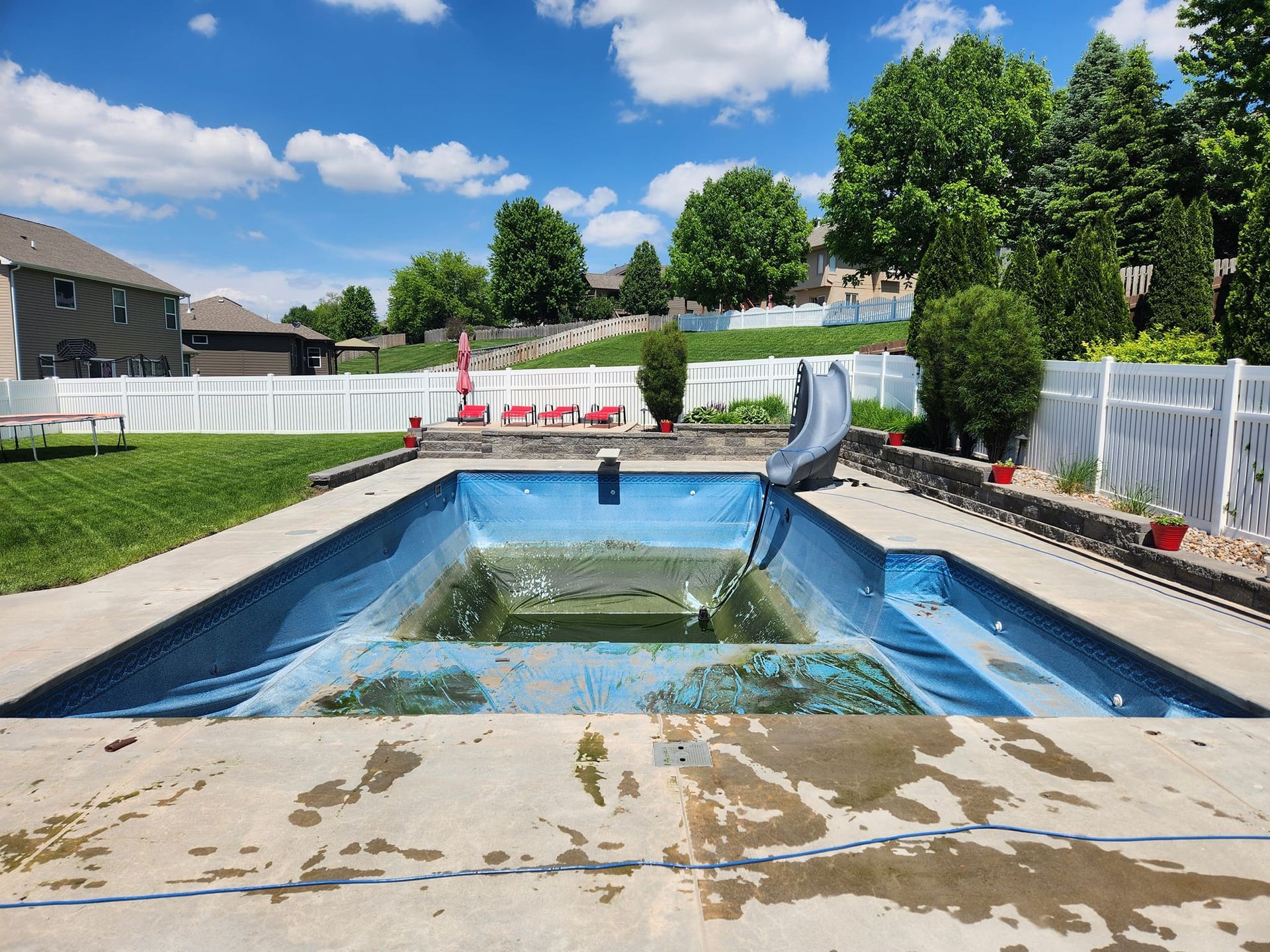 An empty swimming pool with a slide in the backyard.