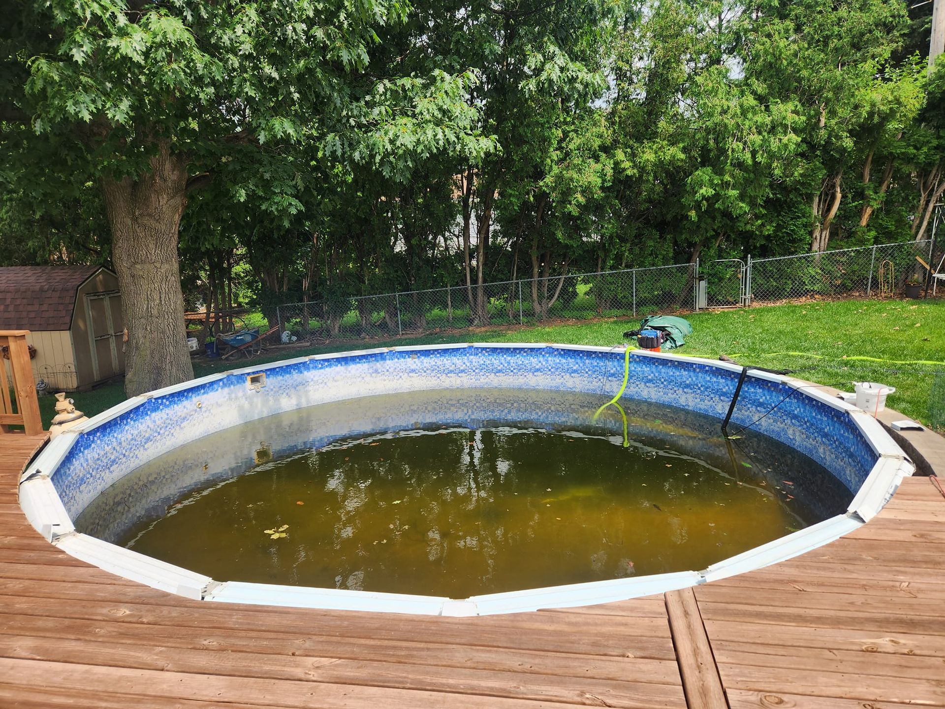 A swimming pool is sitting on top of a wooden deck in a backyard.