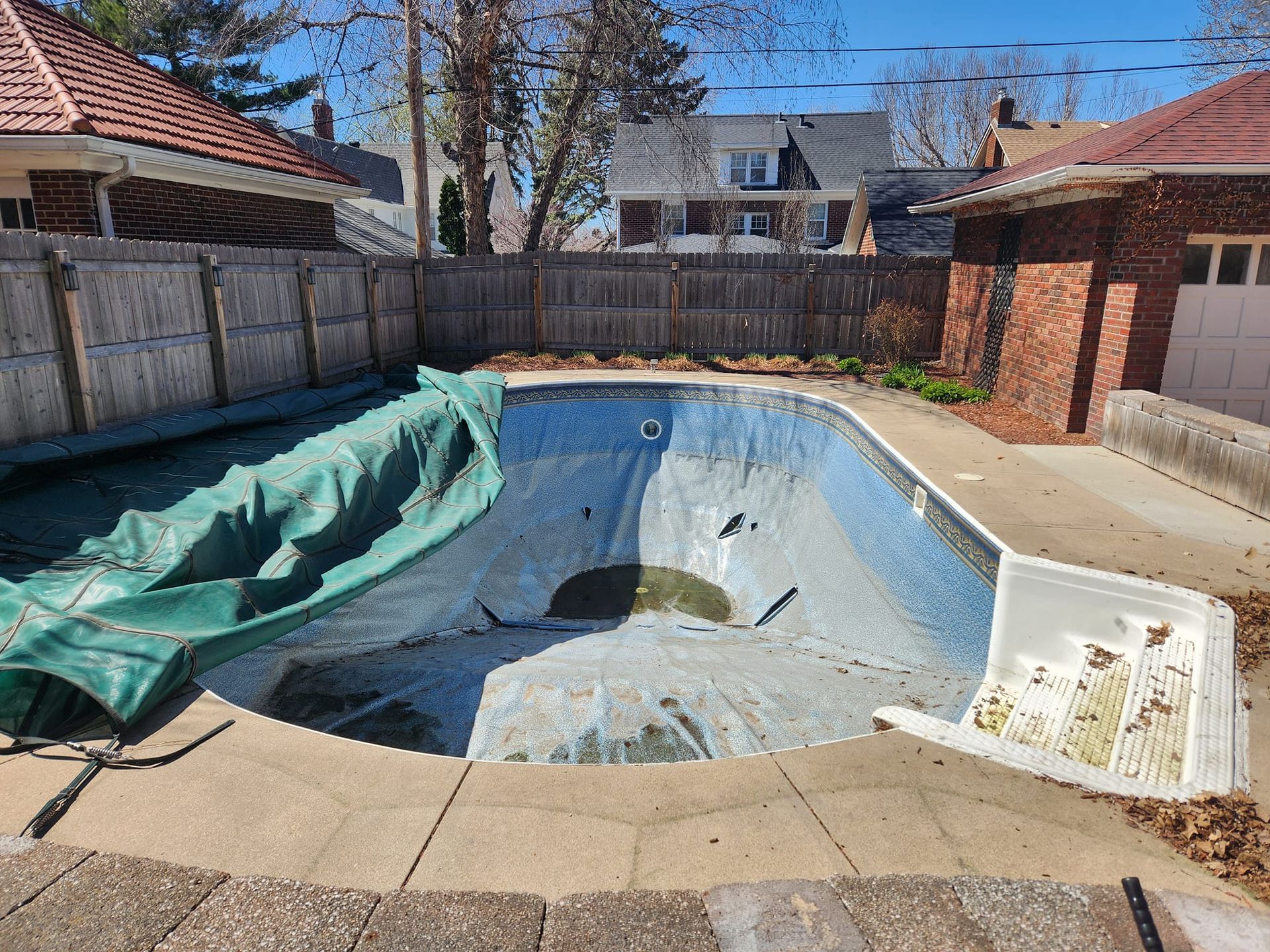 An empty swimming pool is sitting in the backyard of a house.