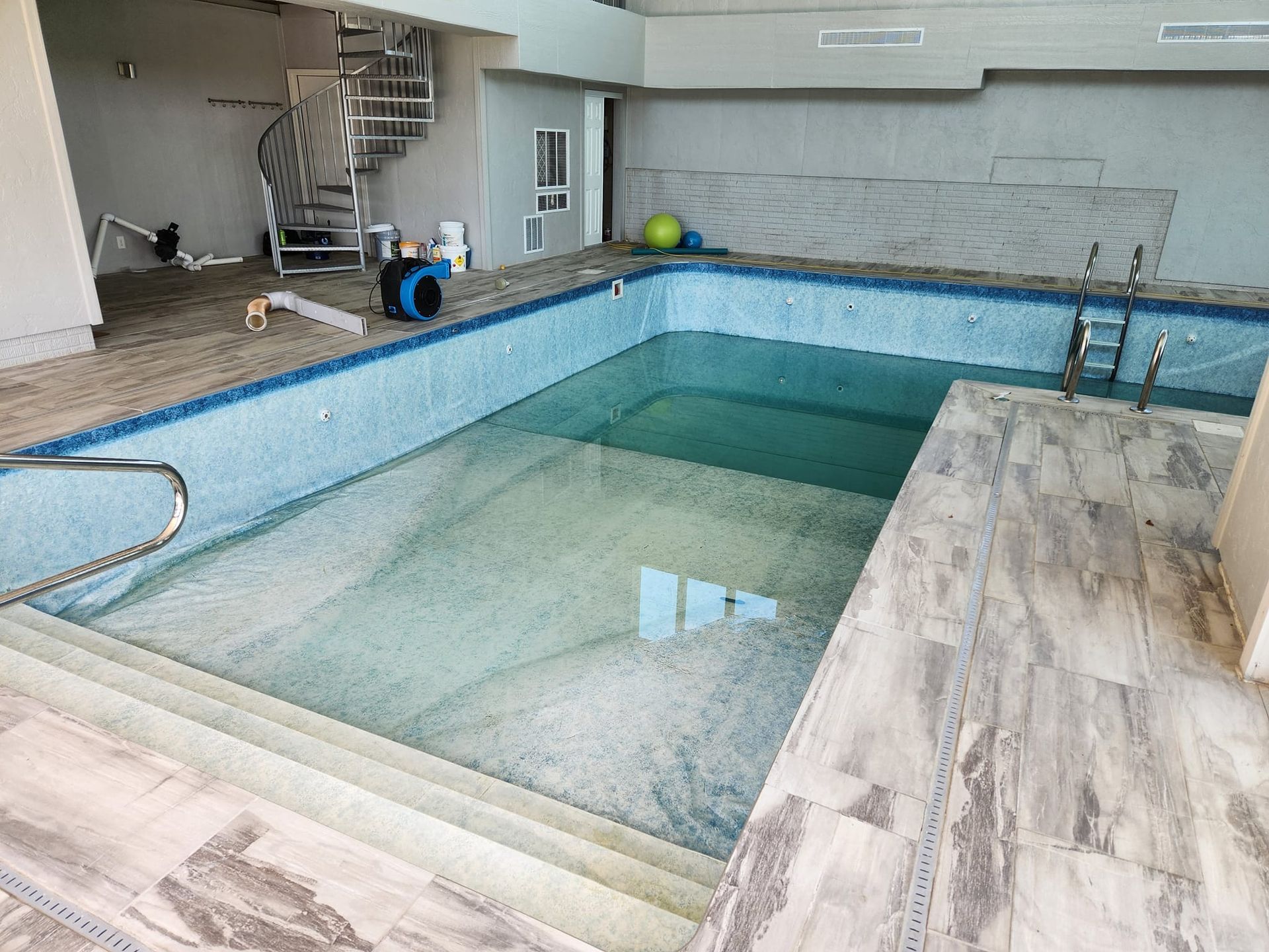 An empty swimming pool with a spiral staircase in the background.