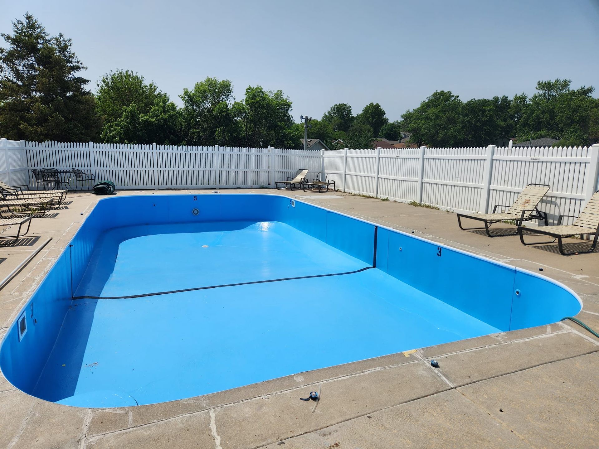 A large blue swimming pool surrounded by chairs and a white fence