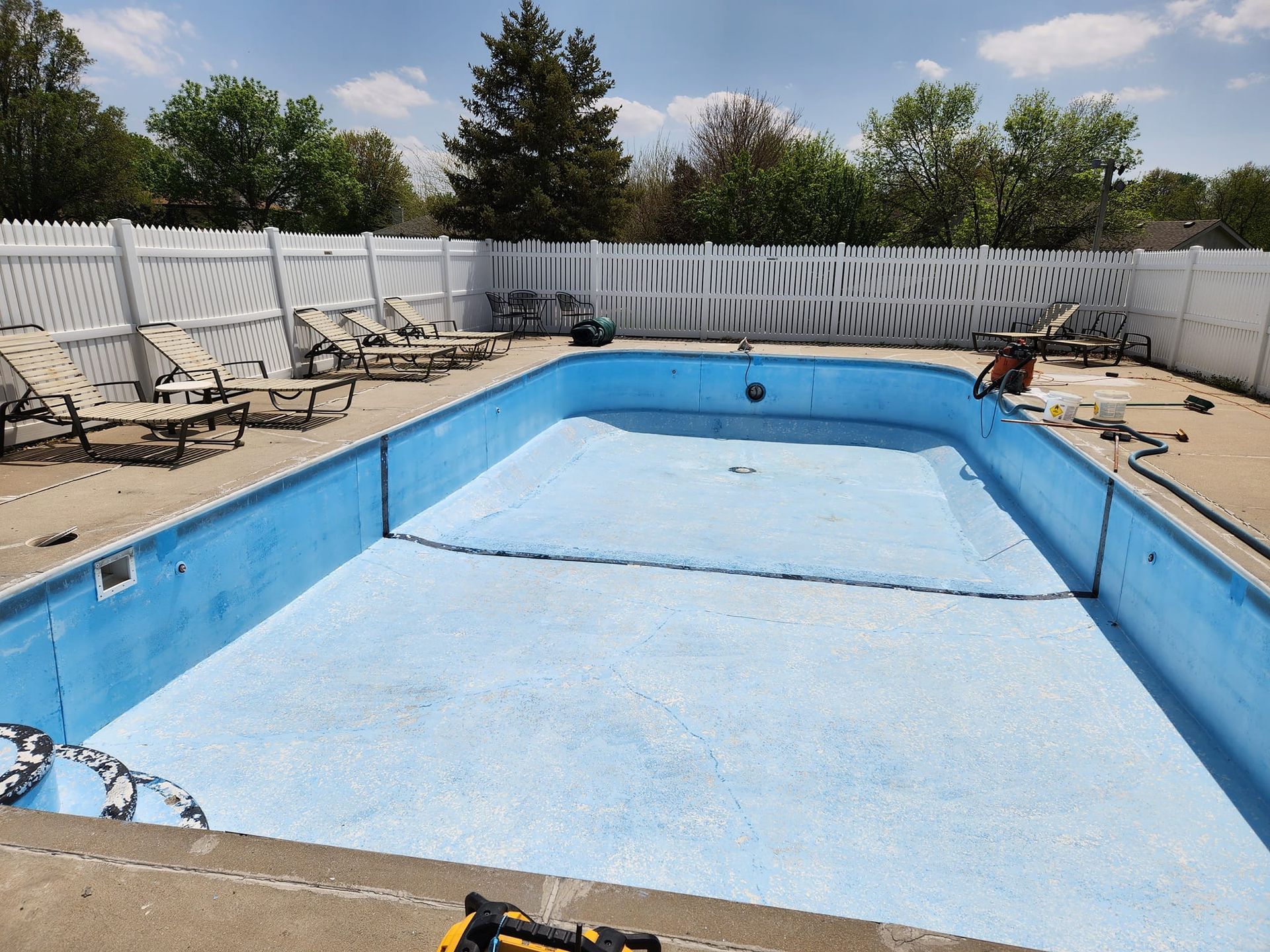 An empty swimming pool with a white fence and chairs around it