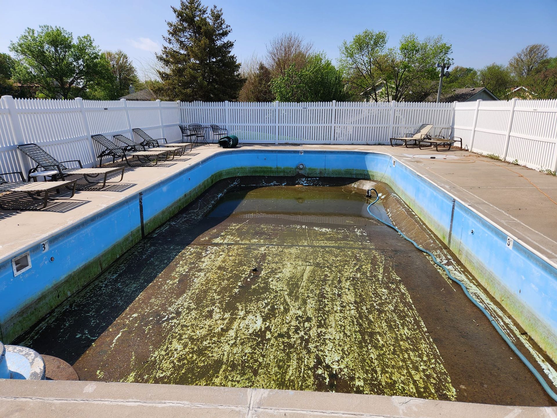An empty swimming pool surrounded by chairs and a white fence
