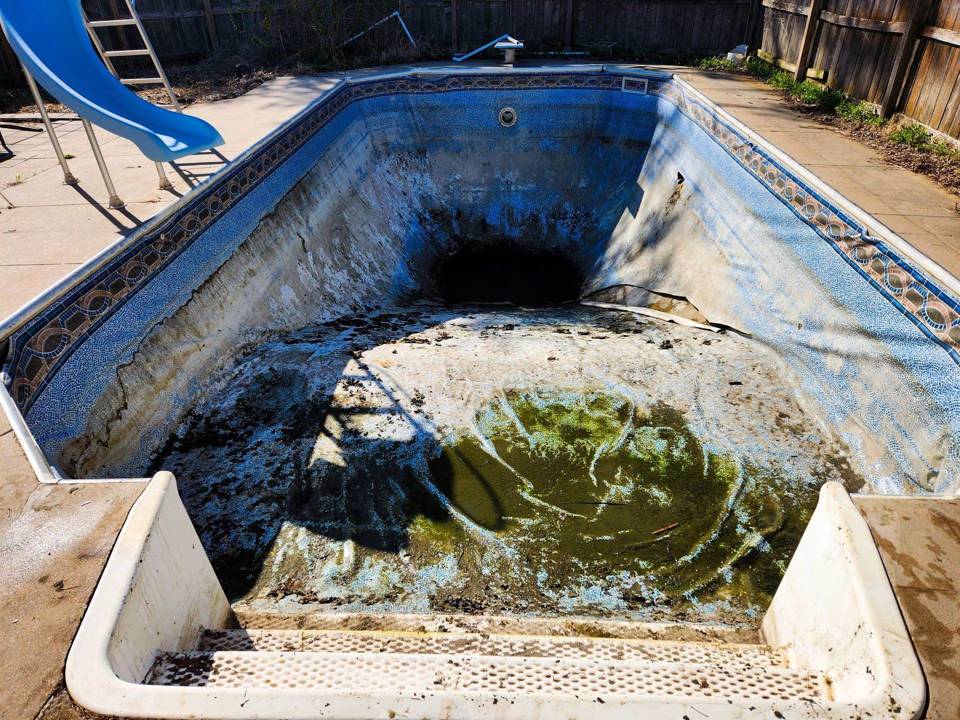 An empty swimming pool with a slide in the background