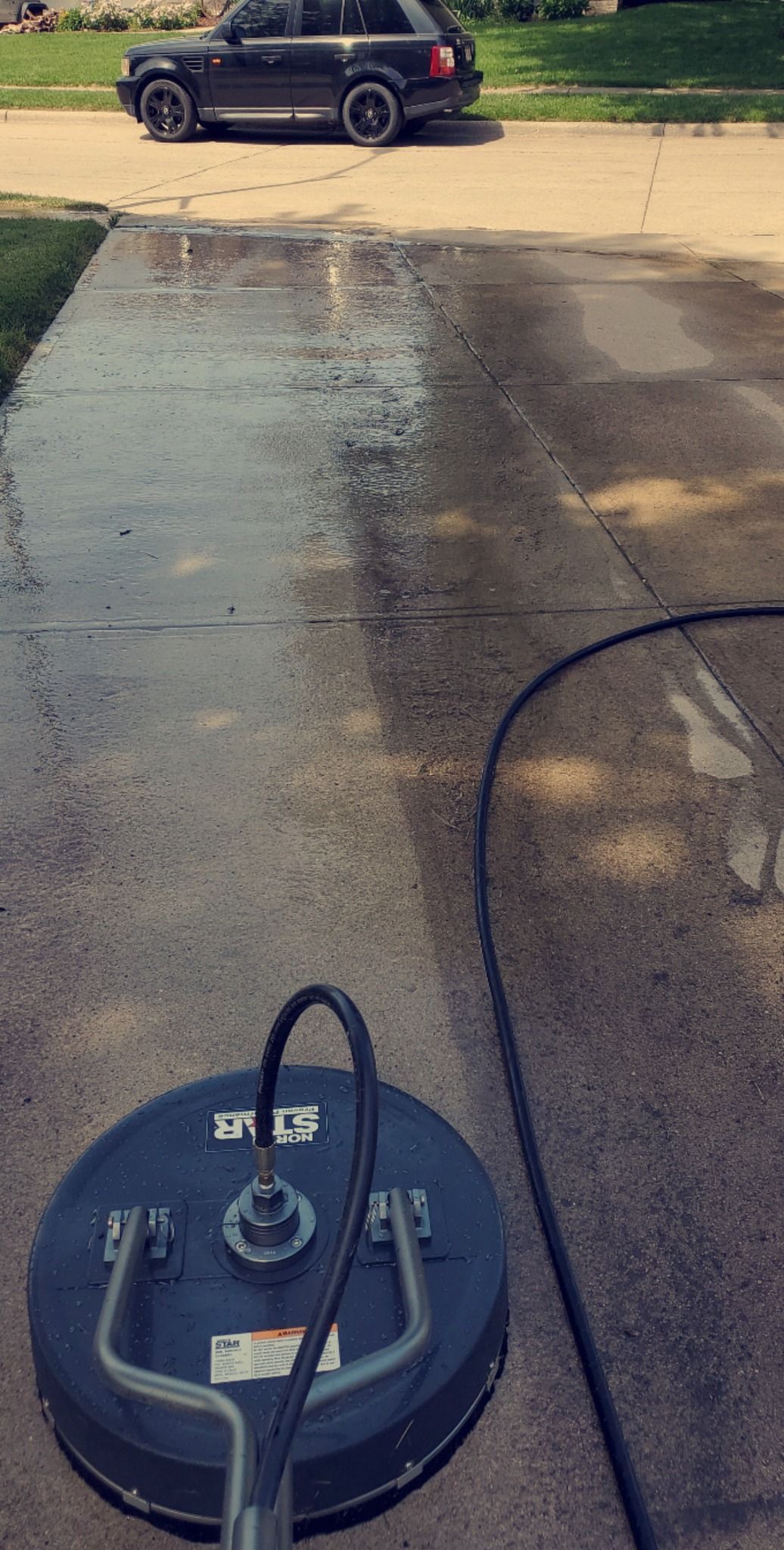 A car is driving down a driveway next to a machine that is cleaning the driveway.