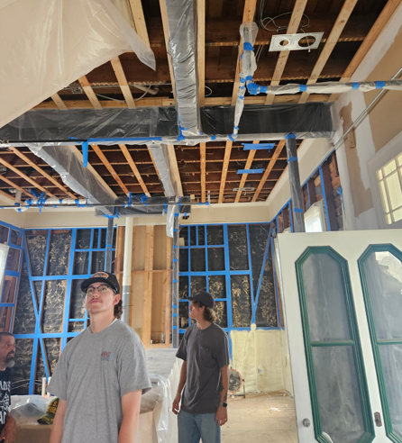 Partially renovated room with exposed ceiling framing and two people looking up at the unfinished work