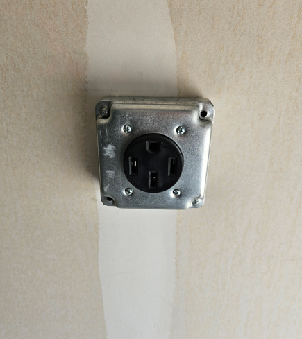 Black wall outlet on a beige wall with a vertical white paint strip behind it
