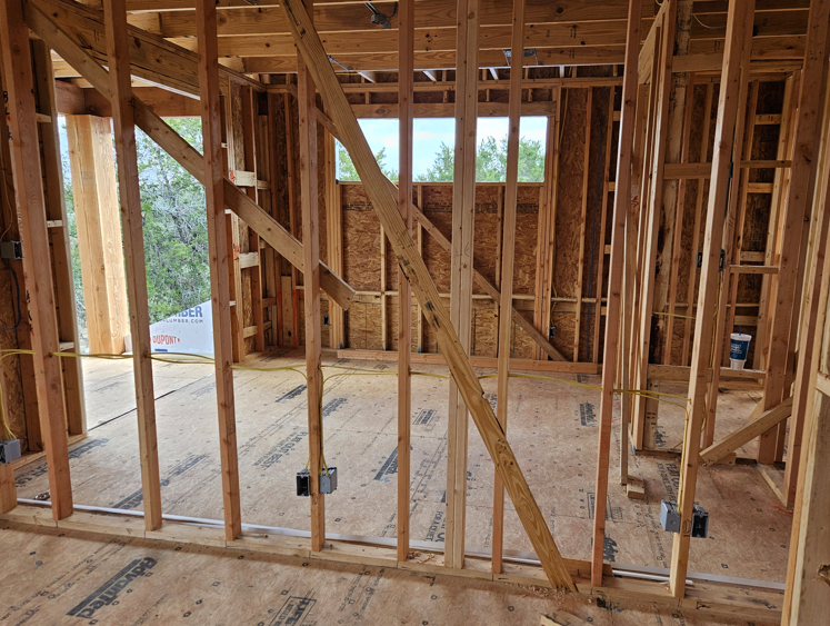Unfinished wooden house interior with exposed framing, beams, and a concrete floor.