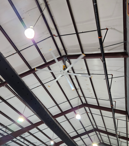 Ceiling with exposed beams, hanging lights, and a large white ceiling fan in an indoor hall