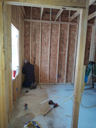 Person installing insulation in a framed room under construction with tools on the floor.