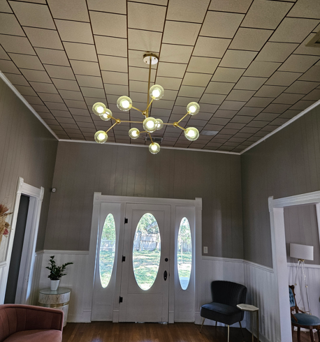 Empty entryway with chandelier, double front doors, gray walls, and white trim.