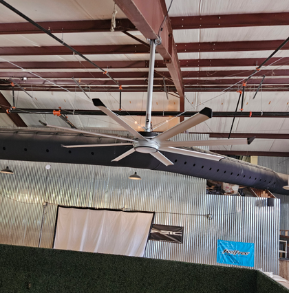 Large black ceiling fan hanging in a corrugated metal hangar interior