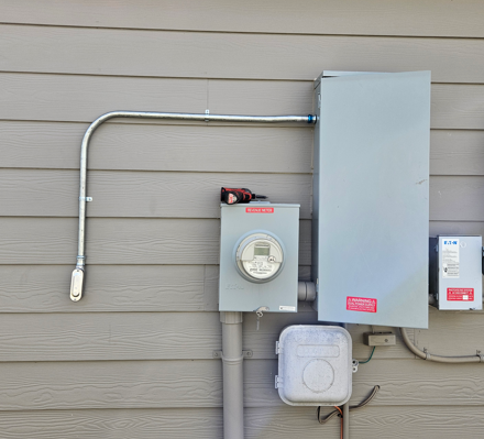 Electrical meter and utility boxes mounted on a tan house exterior wall