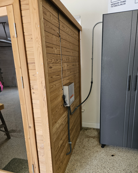 Wooden cabinet beside a gray wardrobe in a cluttered room corner, with cords hanging down.