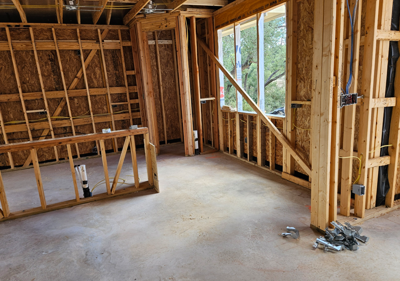 Unfinished house interior with exposed wood framing, concrete floor, and window openings.