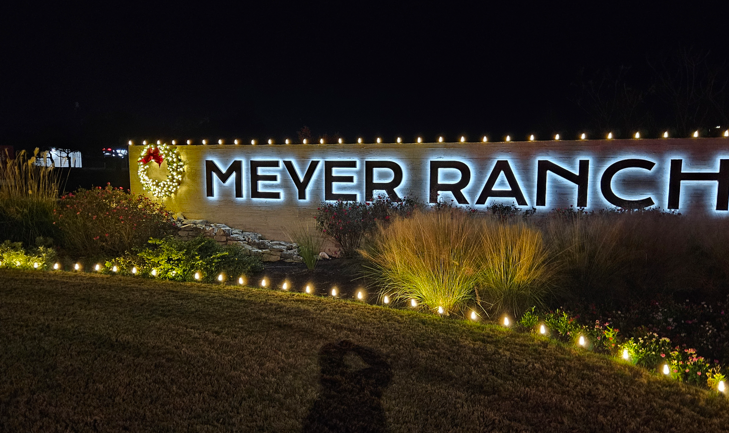 Illuminated “MEYER RANCH” sign at night with landscape lights and shrubs