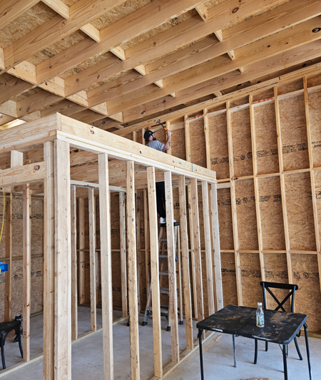 Framed interior of a house under construction with exposed wood studs and ceiling joists.