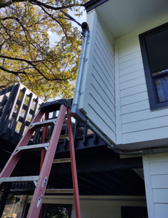 Red ladder beside a house under a raised deck, with white siding and autumn tree branches overhead