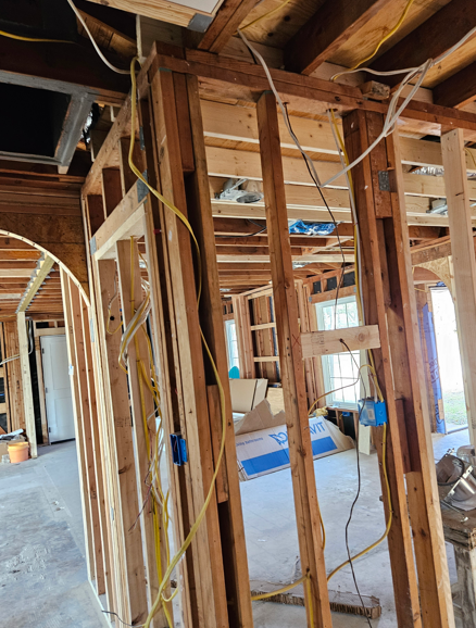 Partially framed interior of a house under construction with exposed wooden studs and hanging wires.