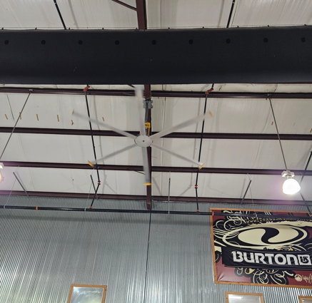 Interior of a metal-roofed building with exposed beams, a hanging light, and a Burton snowboard banner