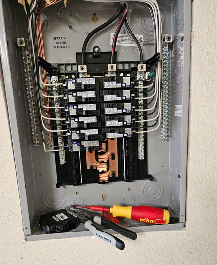 Open electrical breaker panel with many circuit breakers and tools lying at the bottom.