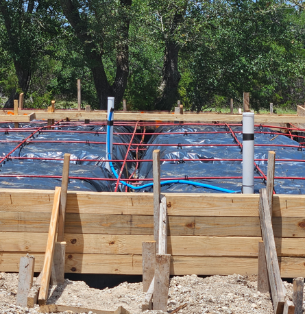 Concrete foundation under construction with red rebar, blue plastic sheeting, and wooden forms outdoors