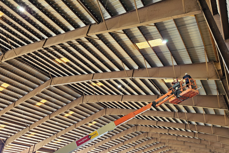 Worker on an orange lift inspecting the high ceiling of an industrial warehouse