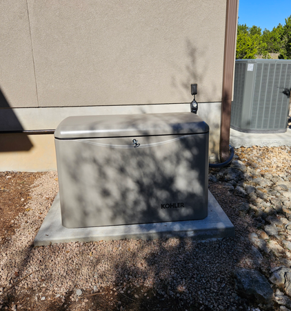 Gray outdoor generator unit beside a beige house wall on a concrete pad, with gravel and shadows nearby