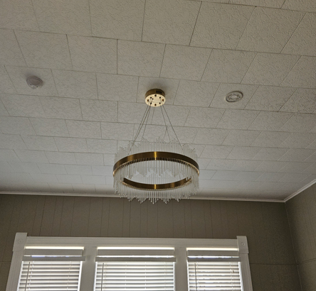 Ceiling light fixture hanging above windows in a room with white ceiling tiles.