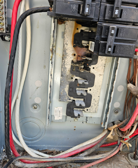Open electrical breaker panel with wires and signs of rust and burn damage on the center bus bars