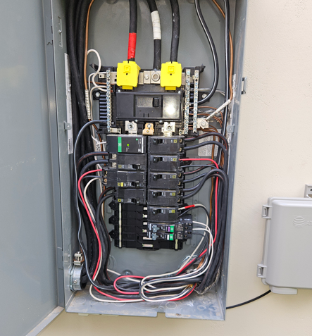 Open electrical breaker panel with wires and circuit breakers inside a metal cabinet.