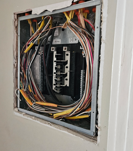 Open electrical panel with bundled multicolored wires in a wall opening