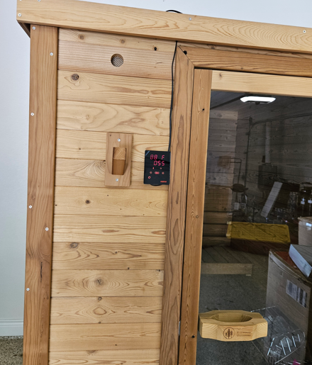 Wooden sauna wall with a digital control panel beside a glass door