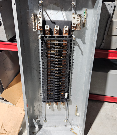 Open electrical breaker panel with rows of circuit breakers and wiring inside a gray metal box.
