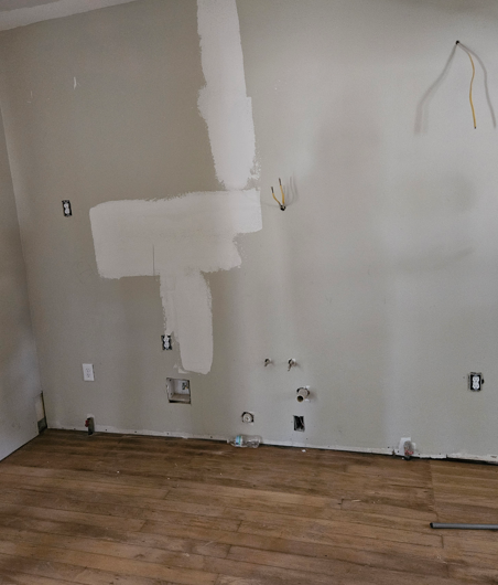Partially painted wall with electrical outlets above a wood floor in an empty room