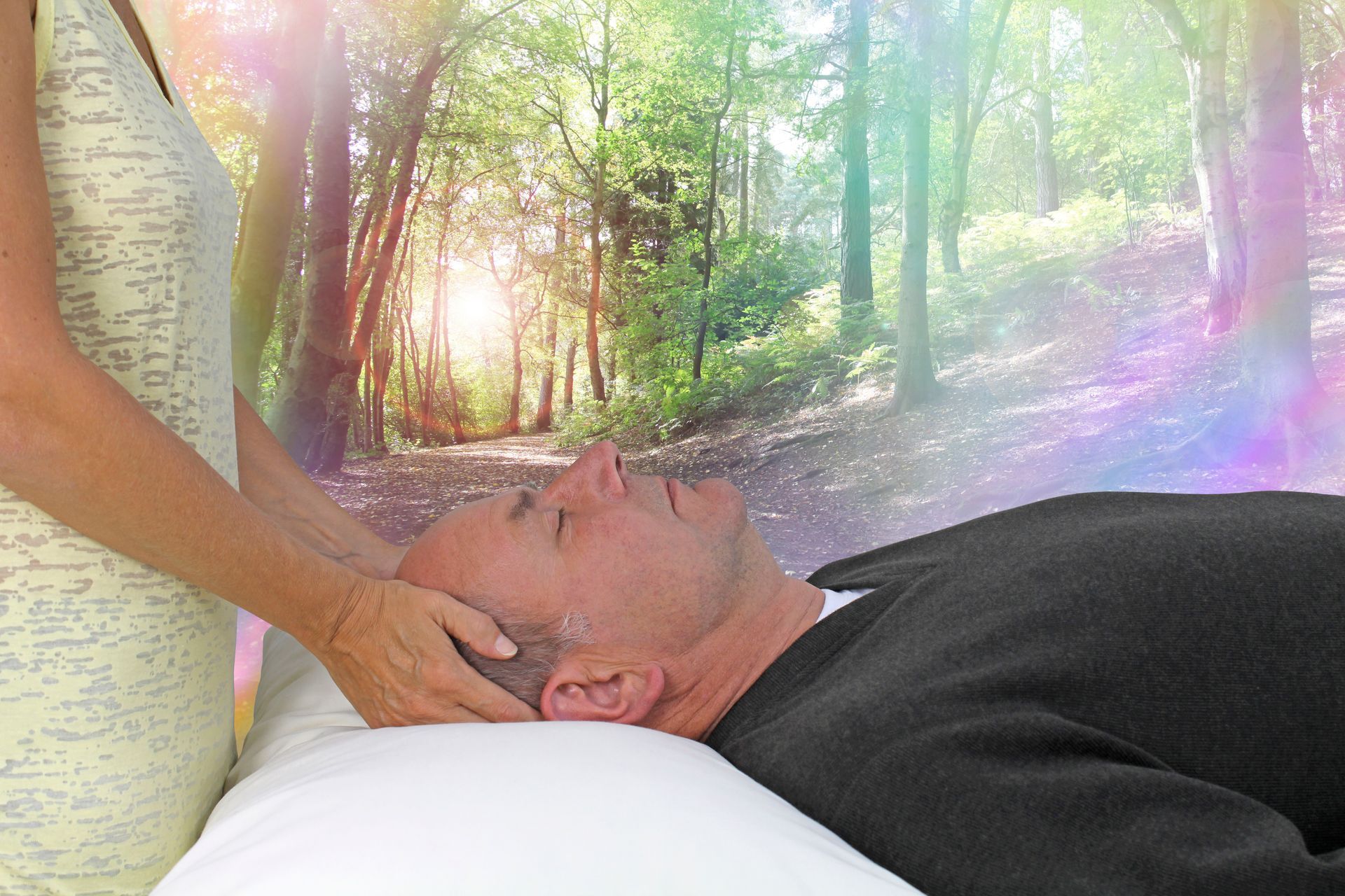 Woman's hands on man's head; lying down on a white bed. Forest background with colorful light beams.