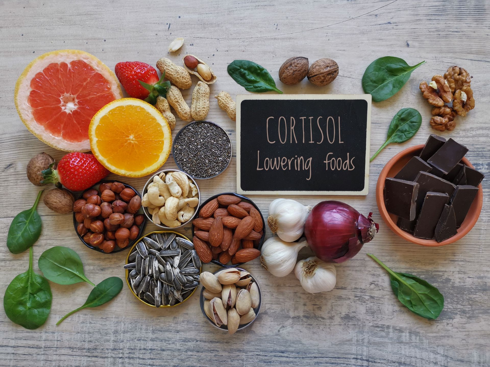 A still-life of foods labeled “Cortisol Lowering Foods” including fruits, nuts, seeds, and dark chocolate.