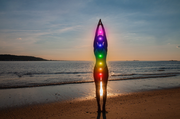 Silhouette of a person on a beach at sunset, with illuminated chakras in rainbow colors along the body.