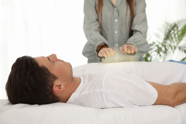 Woman performing energy healing on a man lying on a bed. Glowing light emanates from the woman's hands.