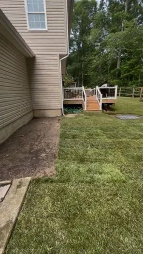 Side view of a beige house with a wooden deck and steps leading down to a freshly laid grass lawn.