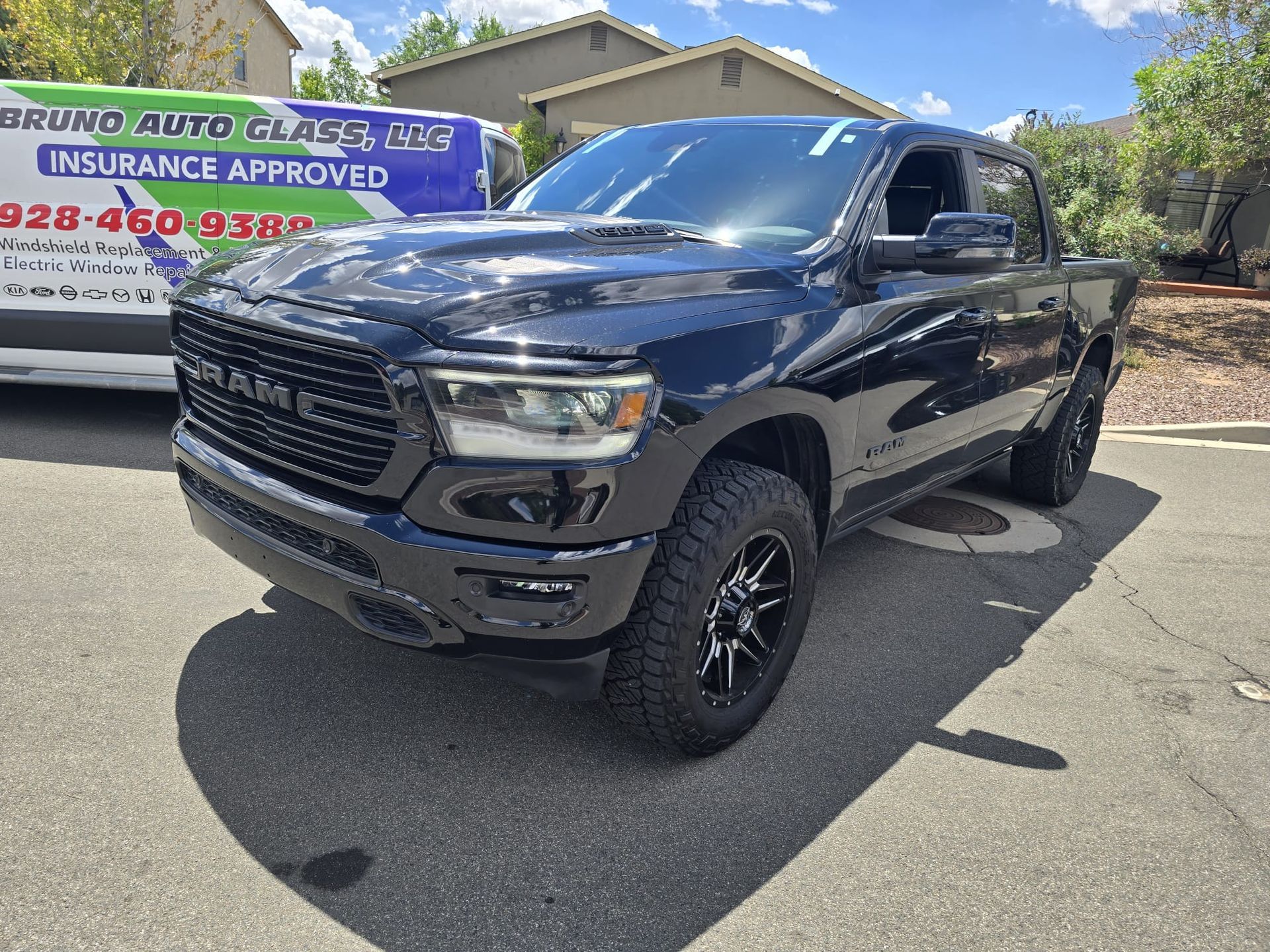 Tow truck with “Bruno Auto Glass” sign parked beside a black RAM truck in a sunny lot