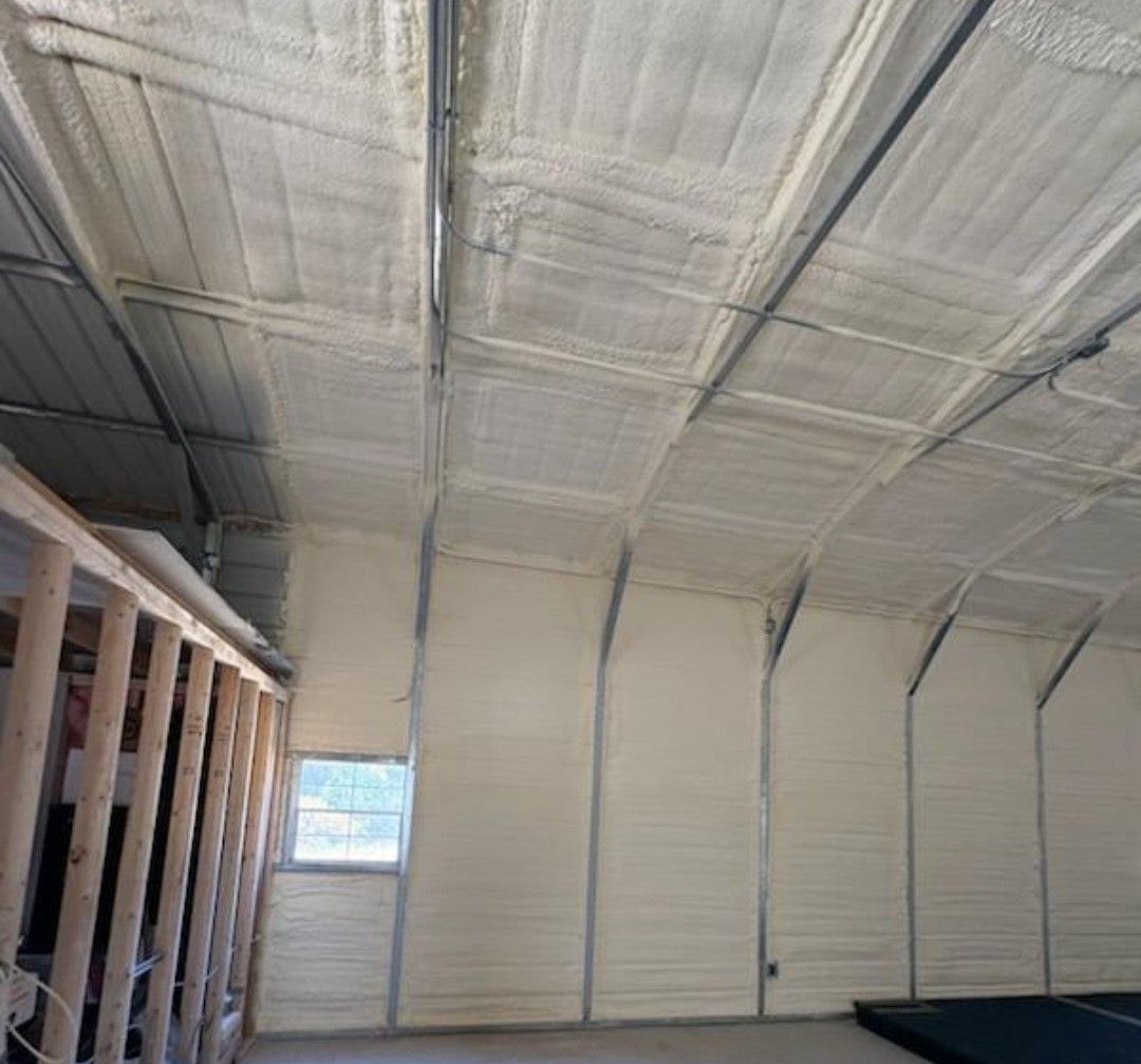 Interior of an unfinished building with insulated ceiling and walls, exposed framing, and a small window.