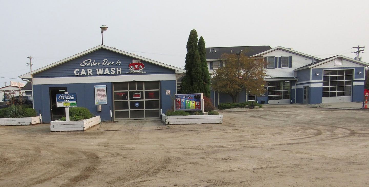 Hand washing a blue car's headlight with a soapy sponge.